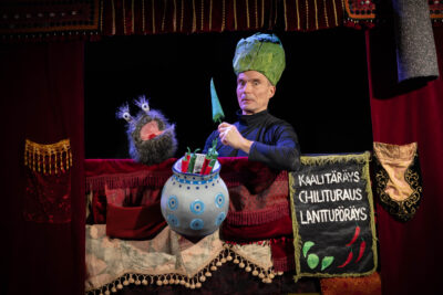 Kuvassa Raxu Taskunen -nukke ja esiintyjä Simo Heiskanen, joka pitää kädessään chiliä hämmentynyt ilme kasvoillaan.