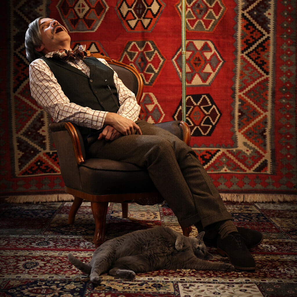 Tuolissa istuu henkilö, joka kuorsaa, hänen jaloissaan makaa selällään harmaa kissa.